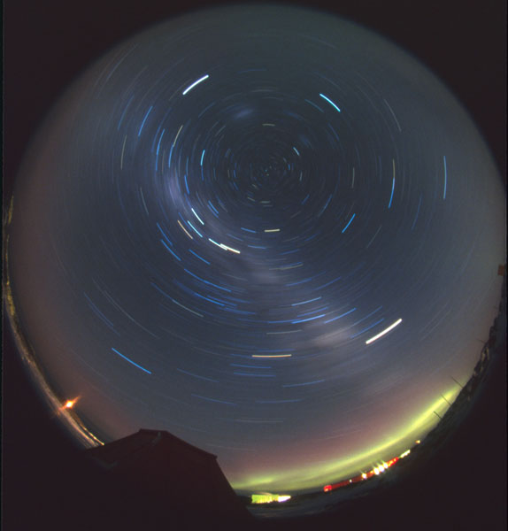Star trails at Casey Station with an aurora on the horizon above the station